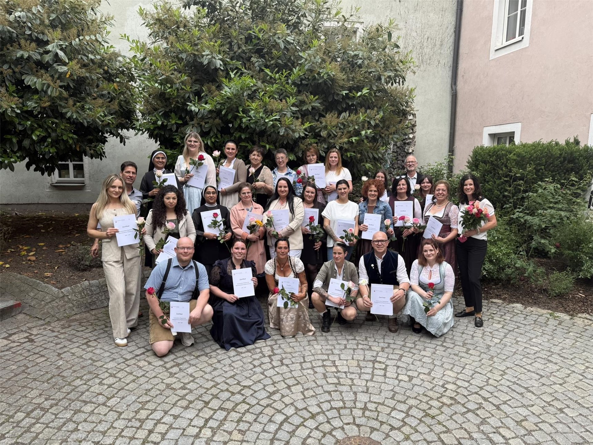 25 Teilnehmende mit Rosen vor dem Eingang der Katholischen Akademie Regensburg. 